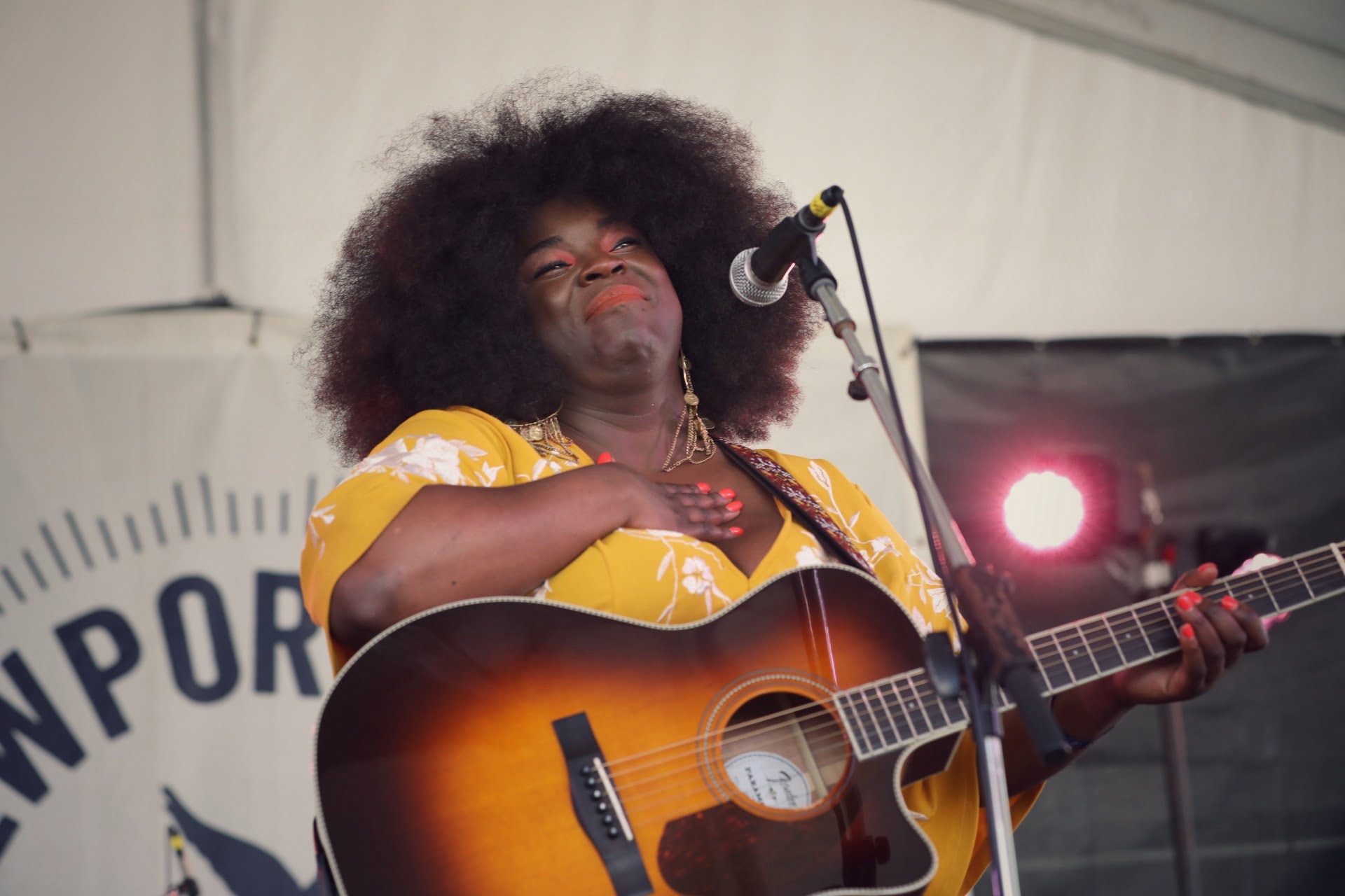 Yola, wearing a yellow dress, places her hand over her heart while holding a guitar at Newport Folk Fest.