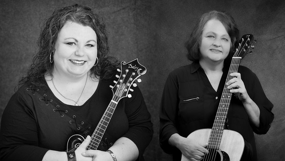 A black and white photo Tina Adair (left) holding a mandolin and Dale Ann Bradley (right) holding a guitar.