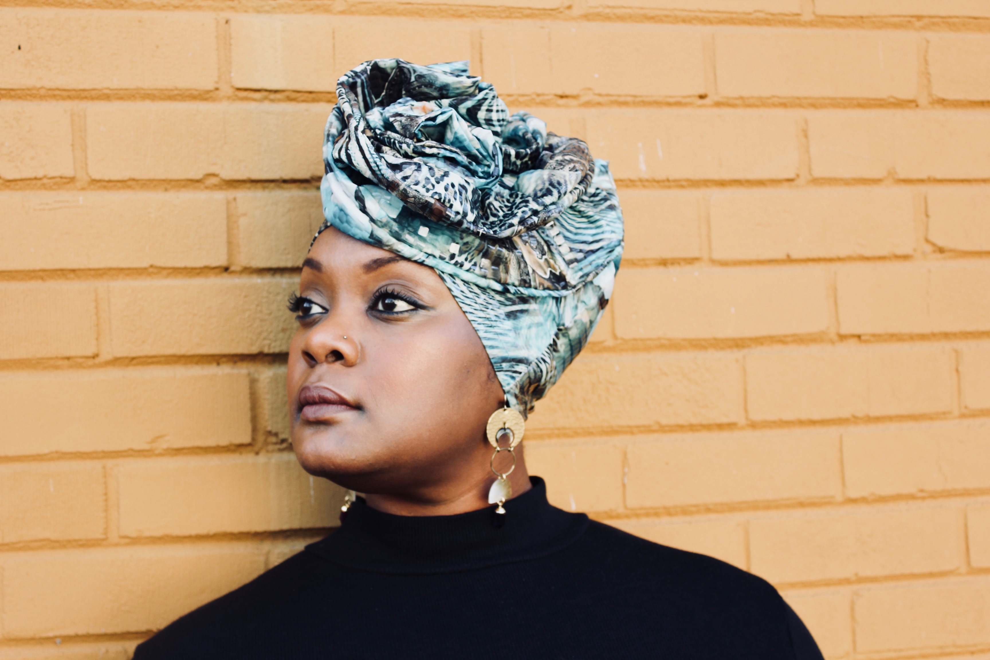 Kyshona with a colorful headscarf standing in front of brick