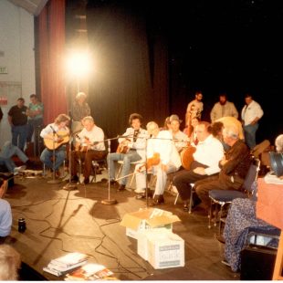 A workshop held at the first MerleFest in 1988. (L-R:) Jack Lawrence, Doc Watson, Marty Stuart, Jim Shumate, Earl Scruggs, Grandpa Jones. David Holt behind the first row of musicians, Ramona Jones on the far right, partially obscured by camera.