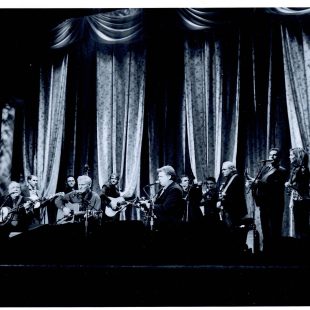 Earl Scruggs, Doc Watson, Ricky Skaggs, and many more musicians (including John Jorgenson, Cody Kilby, Mark Fain, Andy Leftwich, Alison Krauss, Jim Mills, and more) onstage filming 'The Three Pickers.'